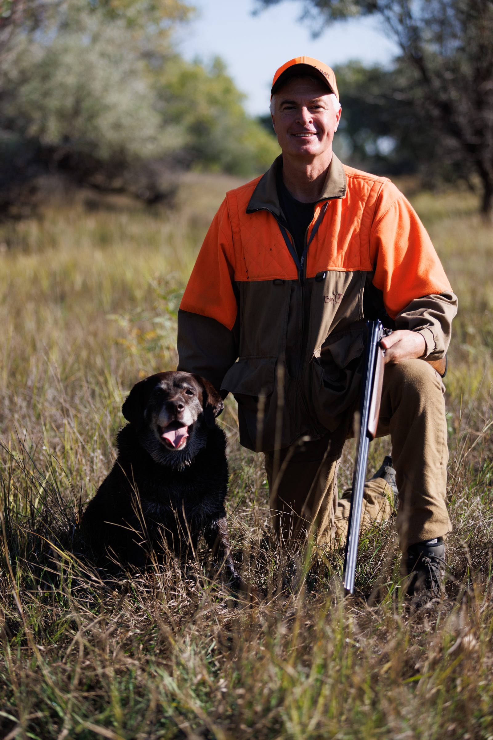 Marty Jackley kneeling in blaze orange with his lab Remi and his shotgun